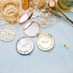 three compact mirrors sitting on top of a table next to some dried flowers and leaves