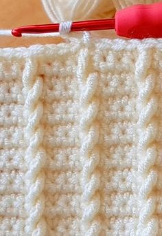 the crochet stitch is being worked on with a red handled knitting needle in front of it