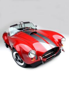 a red sports car with black and white stripes on the hood is parked in front of a gray background