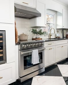 a kitchen with marble counter tops and stainless steel stove top oven, white cabinets, and black and white checkered flooring