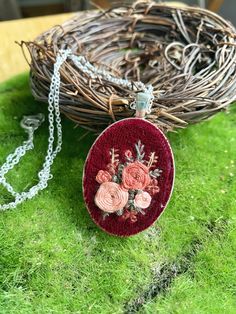 a necklace with flowers on it sitting in the grass next to a bird's nest