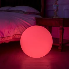 an illuminated ball sits on the floor next to a bed in a room with pink lighting