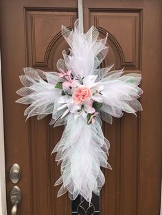 a cross made out of feathers and flowers on a front door with a pink rose