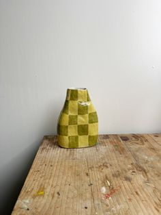 a yellow vase sitting on top of a wooden table next to a white wall and floor