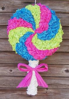 a lollipop is hanging on a wooden fence with pink, blue, and green yarn