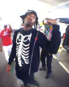 a man wearing a skeleton shirt and hat is on his skateboard in an airport