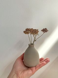 a hand holding a small white vase with flowers in it's top and bottom