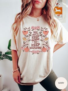 "🌸 Elevate your boho chic style with our Fashionable Boho \"You Gotta Keep Going To Keep Growing\" Women's Shirt! 🌿 Indulge in the perfect blend of fashion and comfort with this trendy shirt featuring a vibrant flower design. Embrace the bohemian spirit and empower yourself with the inspiring message gracefully woven into the fabric. Here's why this shirt is a must-have: ✨ Flower Design: Adorned with a chic and lively flower design, this shirt captures the essence of bohemian beauty. Let the floral details enhance your style and bring a touch of nature's charm to your wardrobe. 🎨 12 Vibrant Color Options: Express your individuality with a spectrum of 12 stunning colors. From soft pastels to bold and vibrant shades, find the perfect hue that resonates with your unique sense of style. 🌻 Boho T Shirt Design, Spring Bohemian T-shirt With Graphic Print, Hippie Printed Crew Neck Top, White Floral Print Hippie Top, Bohemian Cotton Tops With Graphic Print, Spring Bohemian T-shirt With Screen Print, Bohemian Crew Neck T-shirt For Spring, Hippie Style Graphic Print Spring Tops, Hippie Graphic Print Tops For Spring