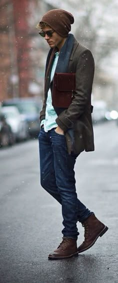 a man standing on the side of a road wearing a jacket and hat with his hands in his pockets