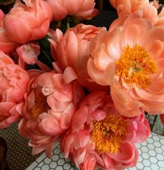 pink and yellow flowers in a vase on a table with a tile floor behind them