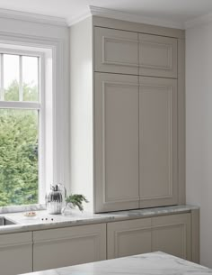 a kitchen with white cabinets and marble counter tops next to a window that has trees in the background