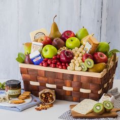 a wooden basket filled with lots of different types of fruit and cheese on top of a table