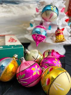 some ornaments are sitting on a table next to a box and a christmas tree in the background