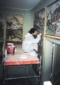 a woman sitting on top of a red table in front of pictures and paintings behind her