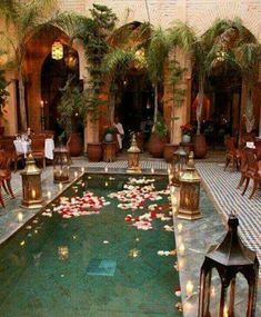 an indoor pool with candles and flowers on the water in front of some people sitting at tables