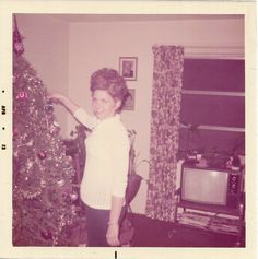 an old photo of a woman standing next to a christmas tree in her living room