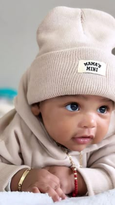 a baby laying on its back wearing a white hat with the name tamba in it