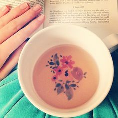 a person reading a book and holding a cup of tea in front of an open book