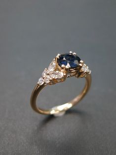 a yellow gold ring with an oval blue sapphire surrounded by small white diamonds on a gray surface