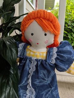 a doll with orange hair is sitting next to a potted plant