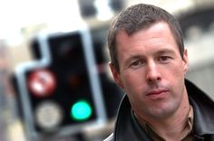 a man is standing in front of a traffic light and looking at the camera while wearing a leather jacket