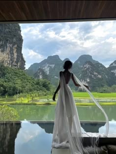 a woman in a white dress standing by a lake