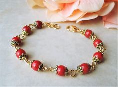 This elegant bracelet features red coral natural stones. Each flanked with decorative bead-caps plated in 24 karat gold. The bracelet is adjustable from 7" to 8" and is finished with a secure gold lobster claw clasp. This colorful bracelet is unique, feminine and eye-catching, Perfect for anyone that wants to make a statement or a great accent to any wardrobe. Also available in sterling silver plate. Adjustable Red Coral Beaded Bracelets As Gift, Elegant Red Coral Beaded Bracelets For Gift, Elegant Red Coral Beaded Bracelet Gift, Gift Red Coral Bracelet With Gemstone Beads, Red Coral Bracelets As A Gift, Red Coral Bracelets For Gift, Elegant Adjustable Red Coral Bracelet, Elegant Red Coral Adjustable Bracelet, Gold Red Coral Bracelets For Gifts