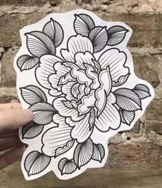 a hand holding up a sticker with black and white flowers on it, against a brick wall