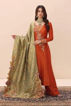 Traditional Orange Embroidered Pakistani Salwar Kameez Dupatta Suit presents a lavishly embroidered pallu that blossoms with intricate floral details. Its beauty is magnified by an array of vibrant precious stones, each one catching the light in a dance of color. The radiance of Swarovski crystals adds to the spectacle, while the bespoke hand-made tassels anchor the piece in a deep tradition of authenticity. Long Kameez: ﻿This Pakistani Long Kameez in raw silk fabric is adorned with fine embroid Orange Contrast Colors Suit, Orange Suits Women Indian, Rust Orange Suit, Suits Women Indian, Outfits Moodboard, Long Kameez, Suite Design, Orange Suit, Suits Pakistani