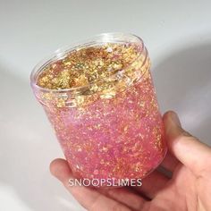 a hand holding a cup filled with pink and gold flecks on top of it