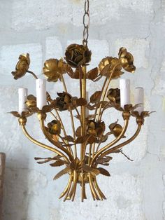 a gold chandelier with five candles hanging from it's center and flowers on the bottom