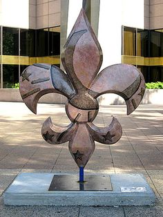 a metal fleur de lis sculpture sitting on top of a sidewalk next to a building