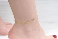 a close up of a person's foot wearing a gold ankle bracelet with two charms on it