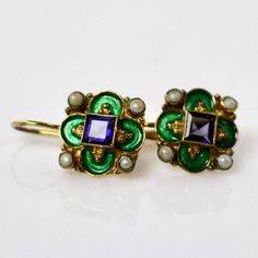 This unique Arts & Crafts Movement design showcases an onyx, iolite, blue topaz, emerald, or garnet set in a cloverleaf of emerald-green or royal blue enamel work, accented with cultured pearl. 24k gold over sterling silver. European back for pierced ears. Size: 3/4 inch. Elegant Enamel Earrings With Gemstones, Elegant Gemstone Earrings With Enamel, Enamel Gemstone Jewelry For Anniversary, Anniversary Enamel Gemstone Jewelry, Elegant Enamel Jewelry With Gemstone, Round Jeweled Enamel Jewelry, Elegant Pierced Enamel Jewelry, Victorian Enamel Jewelry For Formal Occasions, Victorian Enamel Jewelry For Formal Events