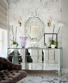 a living room with mirrored furniture and flowers in vases on the sideboard next to a couch