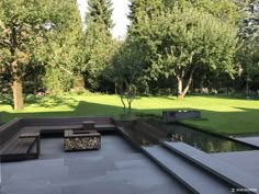 an outdoor seating area with benches and water feature in the foreground, surrounded by trees