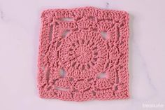 a pink crocheted square on a white surface