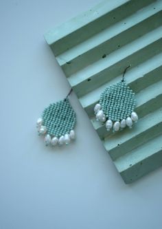 a pair of beaded earrings sitting on top of a piece of green wood next to it