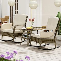 two chairs and a table on a deck with purple flowers in the vase next to them