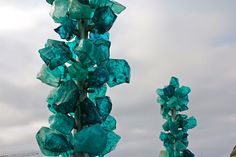 some very pretty blue glass flowers in front of a cloudy sky with buildings behind them