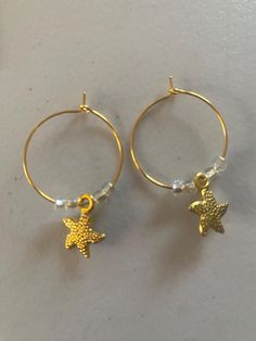 Support the preservation of sea turtles, dolphins, whales, and other marine life by purchasing these simple but beautiful, one-of-a-kind earrings crafted with hypoallergenic loops, alloy charms and West African glass beads. Ocean-inspired Star Earrings For Summer, Summer Star-shaped Ocean-inspired Earrings, Gold Dangle Earrings With Starfish Charm, Summer Ocean-inspired Starfish Earrings, Ocean-inspired Starfish Charm Dangle Earrings, Earring Crafts, Sea Turtle, Starfish, Jewelry Earrings Hoops