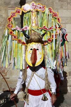 a man wearing a mask and headdress standing in front of a stone wall