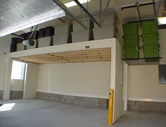 an empty room with several storage bins on the wall and two green barrels hanging from the ceiling