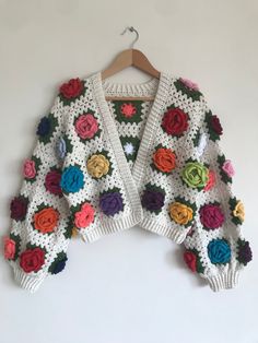 a crocheted sweater with multicolored roses on the front and back, hanging from a hanger