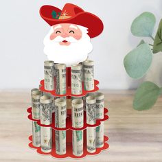 a stack of stacks of money with a santa clause on top and a plant in the background