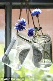 some blue flowers are in a glass jar hanging from a window sill with water