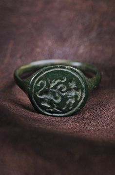 1400-1600s Bronze, patina Size: 19,5mm EU 62,5 Overall: 22,15mm Bezel: 13,15 x 14,5mm Ring height: 23,6mm Weight: 4,0g Condition: Good / wearable Medieval ring with a complex mythical plot. The warrior near the vessel with genies/hookah is a strong ring with a cornered shield and a round shank in cross section. Wearable. Medieval Male Jewelry, Vintage Signet Ring Men, Antique Mens Rings, Medieval Ring, Medieval Rings, Old Rings, Signet Ring Men, Medieval Jewelry, Bronze Patina