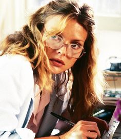 a woman in glasses is writing on a piece of paper and looking at the camera