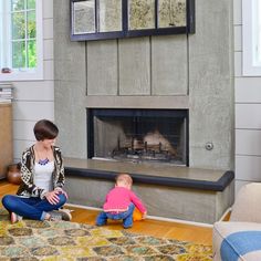 a woman sitting on the floor next to a baby in front of a fire place