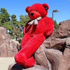 a large red teddy bear sitting on top of a rock